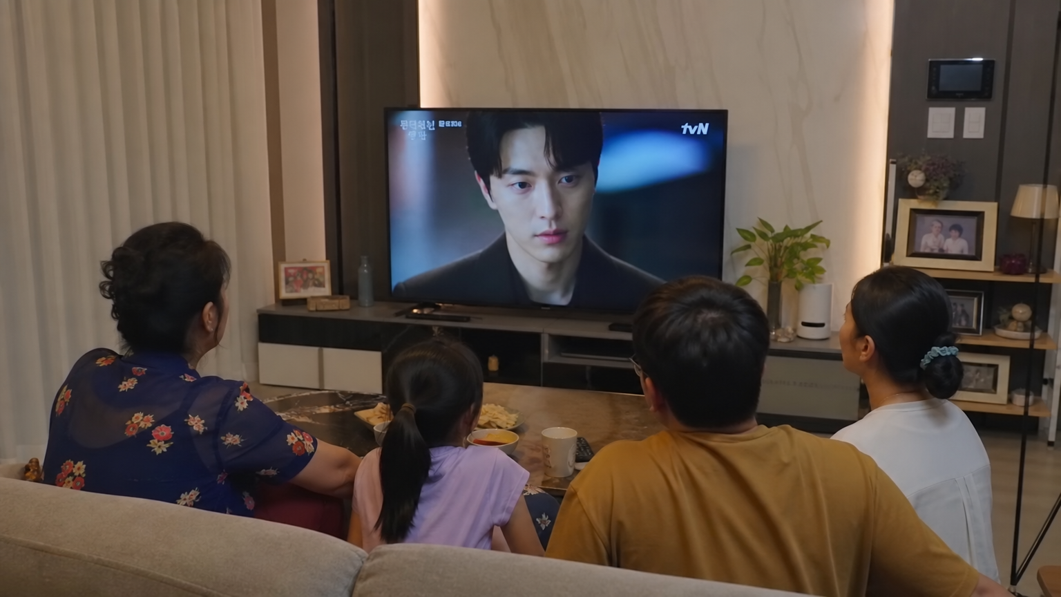 현대적인 거실에서 가족들이 모여 한국 드라마를 시청하는 장면