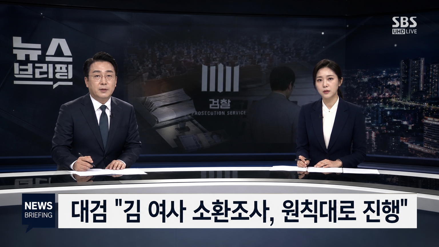 민감한 주제를 논의하는 한국 뉴스 스튜디오에서 진지한 표정으로 앵커들이 대화를 나누는 장면