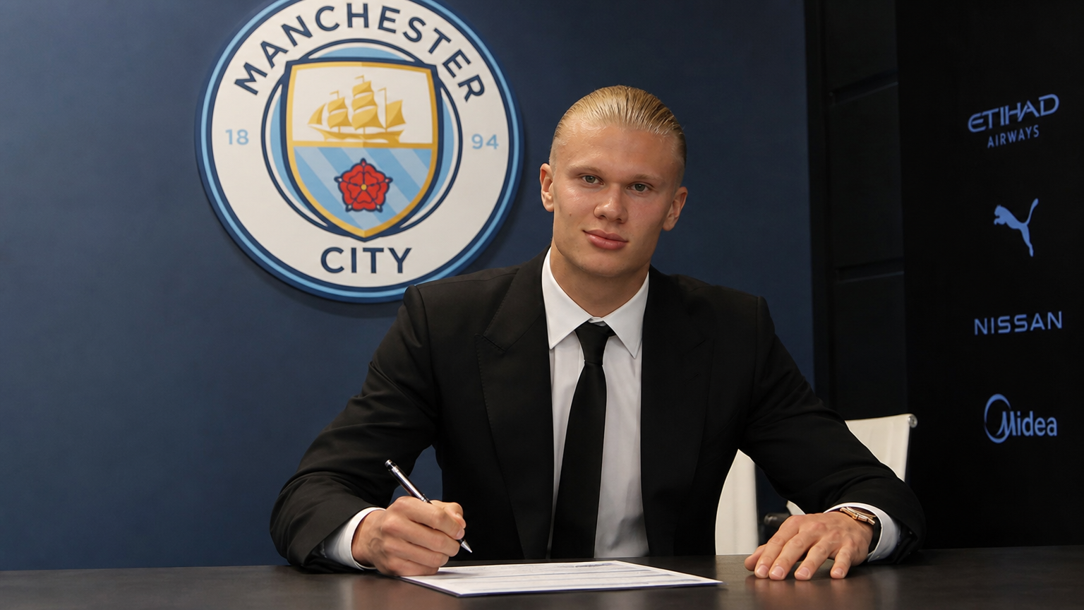 사무실 책상에서 계약서에 서명하는 축구 선수와 배경에 보이는 맨시티 로고