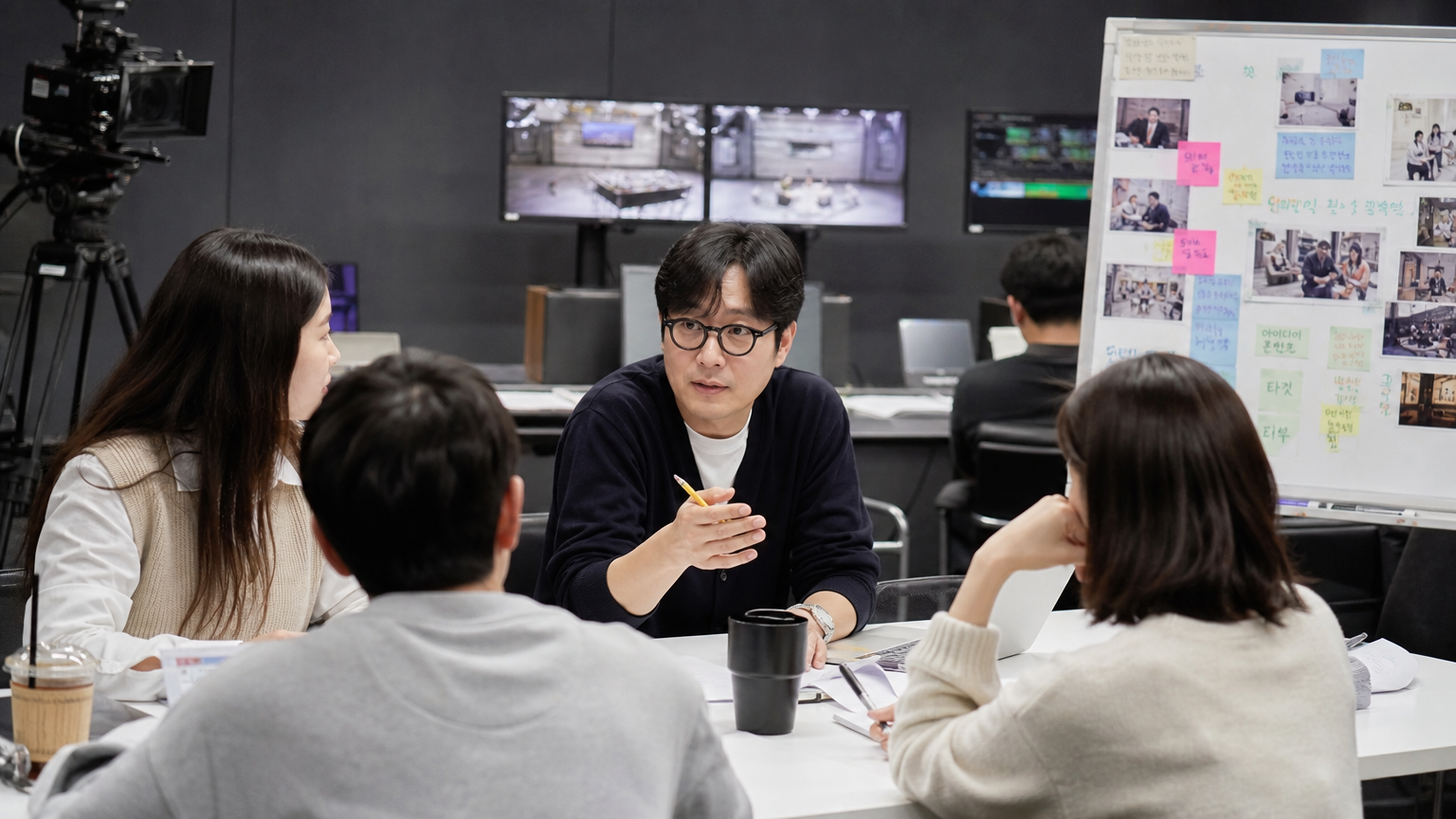 현대적인 스튜디오에서 카메라와 모니터에 둘러싸여 팀과 함께 아이디어를 구상하는 한국 TV 프로듀서