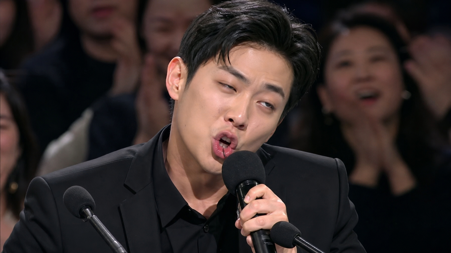 무대 위에서 과장된 성대모사를 하는 한국 배우의 모습