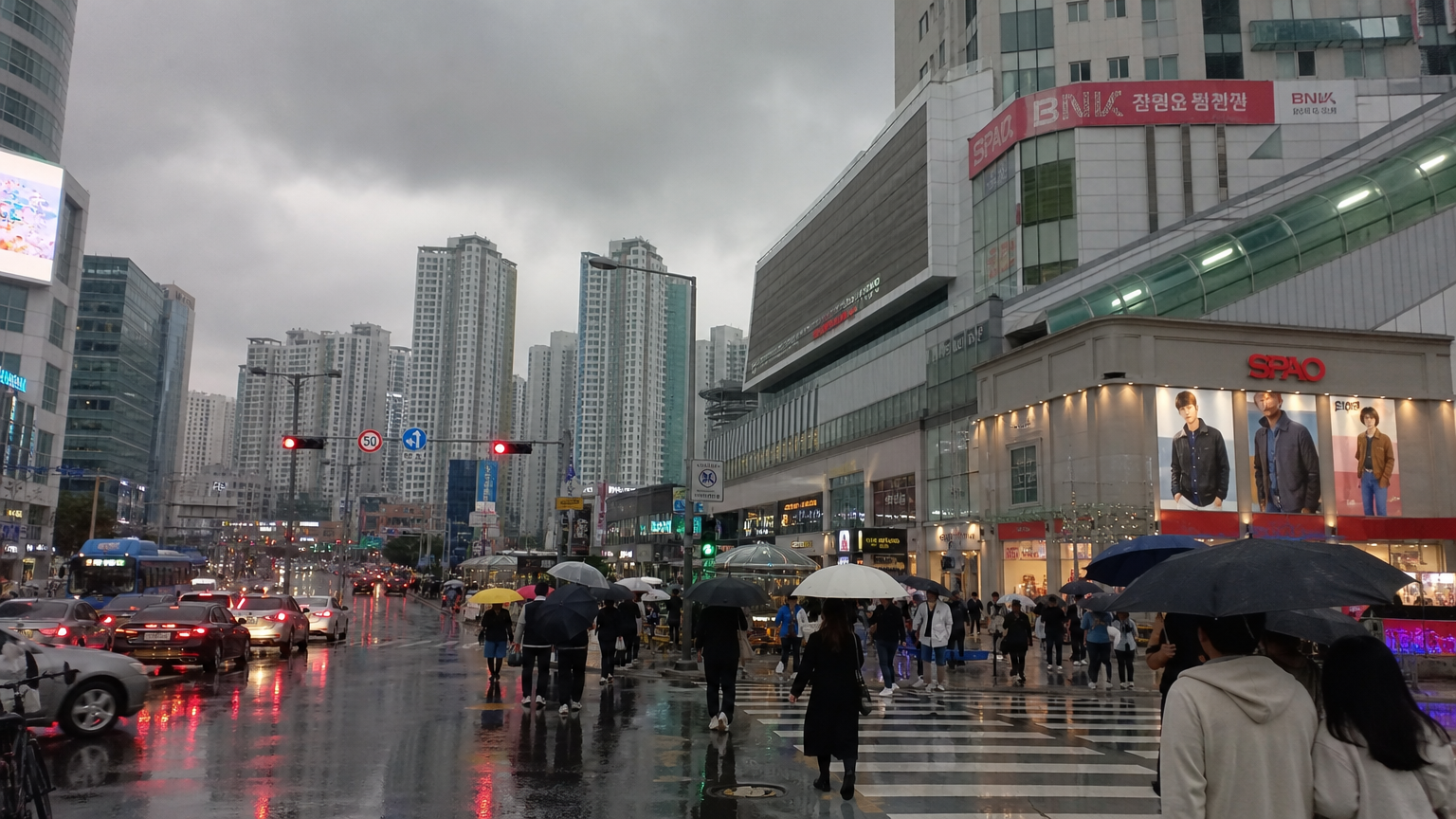 구름 낀 날씨에 우산을 쓰고 바쁜 거리를 지나는 사람들