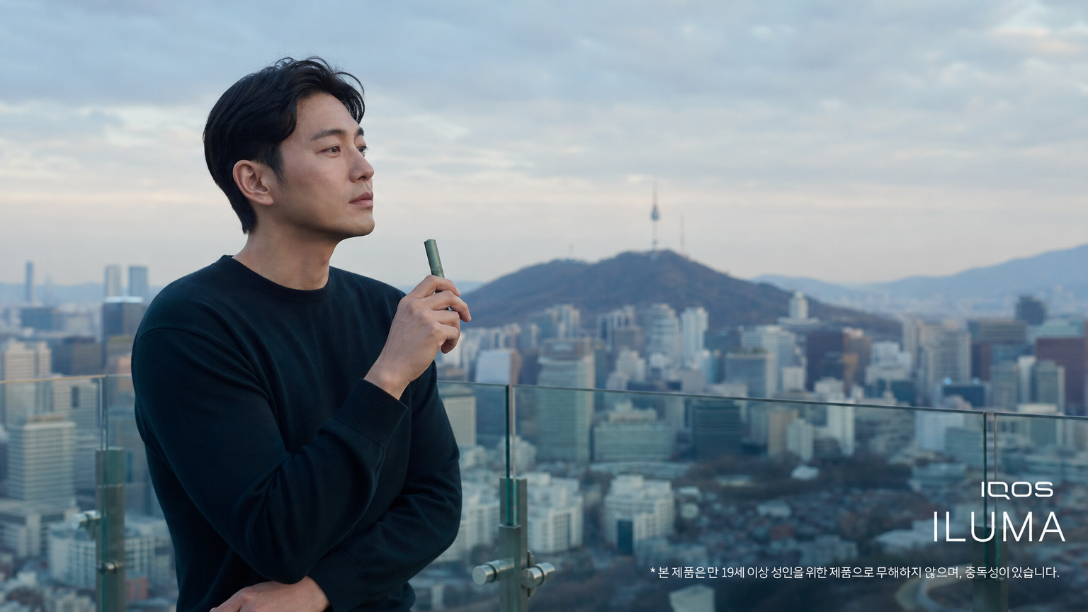 서울 도심 전경을 배경으로 루프탑에 서서 아이코스 일루마를 들고 있는 남성