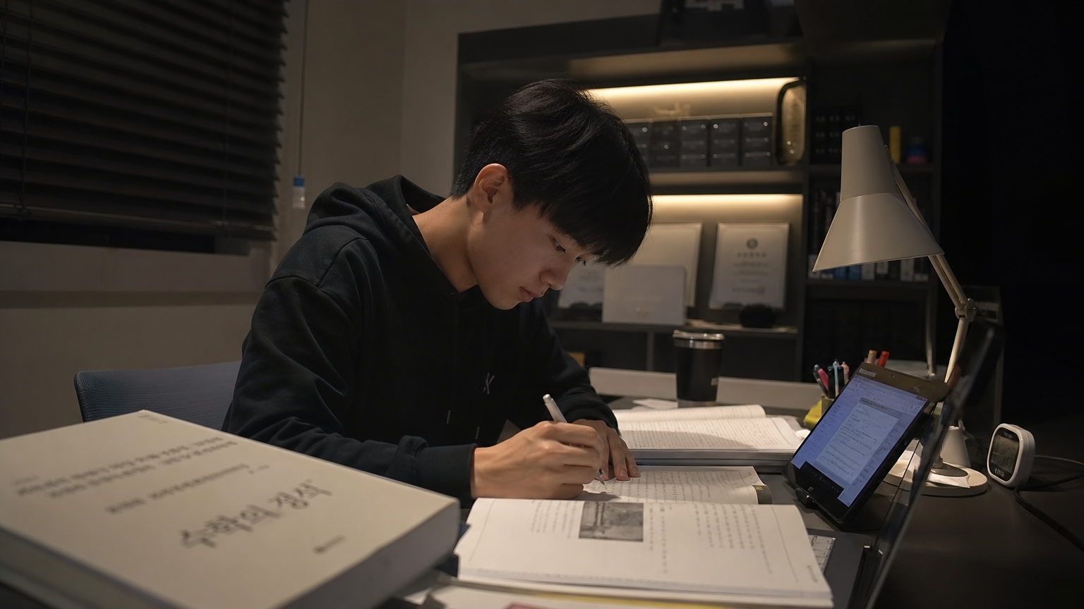 현대적인 방에서 교재와 디지털 기기를 활용해 집중적으로 공부하는 고등학생의 모습